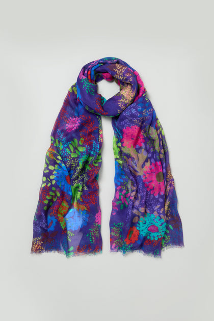 The Bright Blooming Garden Scarf is a silk modal accessory with a vibrant floral pattern in blue, purple, pink, green, and red, shown on a plain light background.