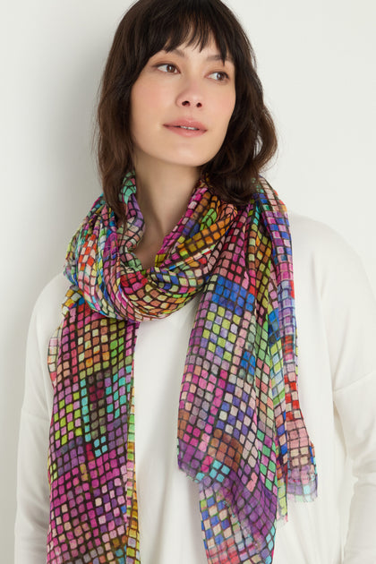 A woman with shoulder-length brown hair wears a white top and the Coloured Glass Tiles Scarf, its mosaic-inspired print draped stylishly around her neck.