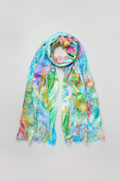 The Dreamy Floral Oasis Scarf is a lightweight modal silk blend with a colorful abstract floral design in blue, green, yellow, and pink tones, shown against a plain background.