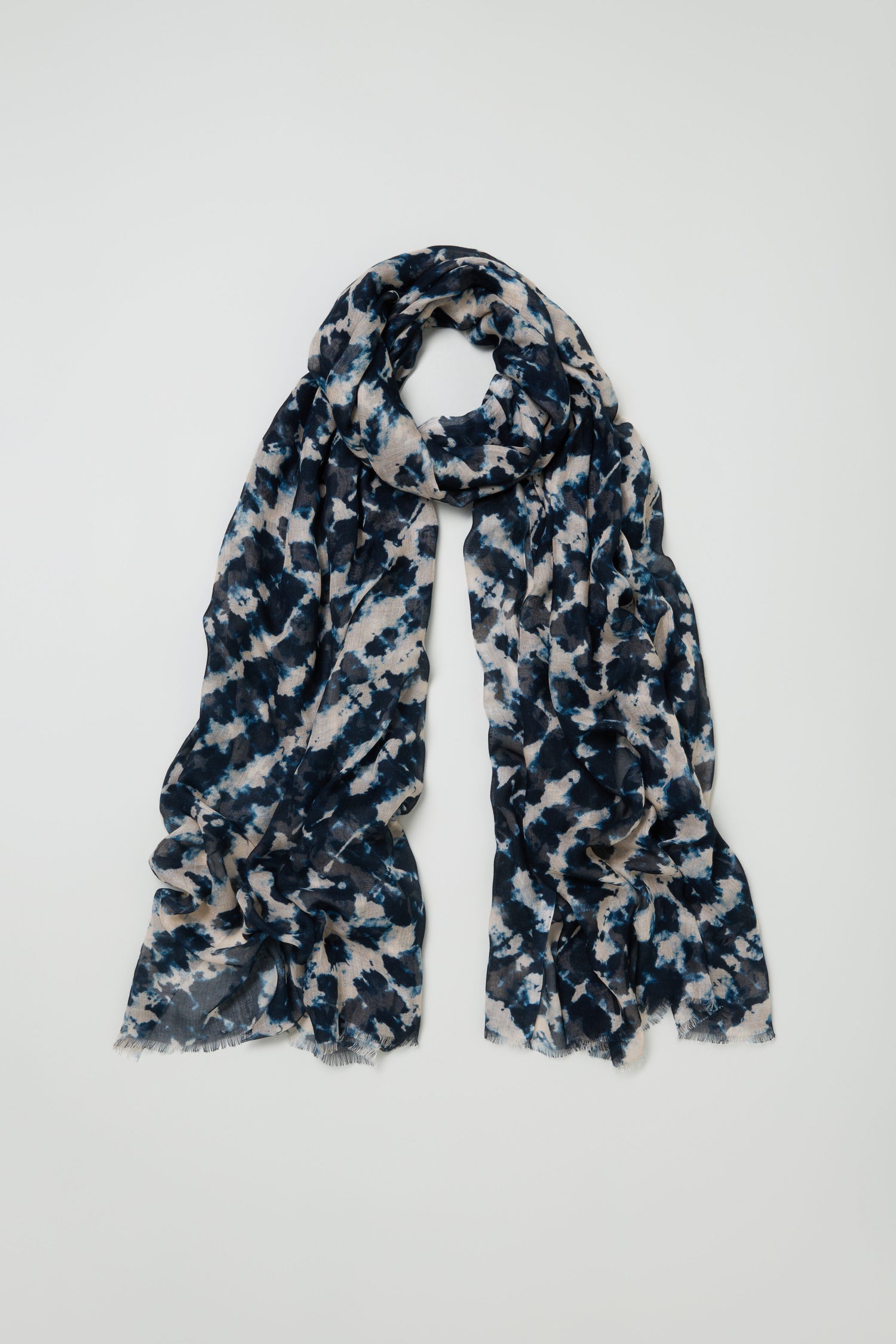 The Diamond Tie Dye Scarf is a long, lightweight modal silk blend with blue, black, and beige abstract patterns, shown loosely looped against a plain white background for a soft, silky drape.