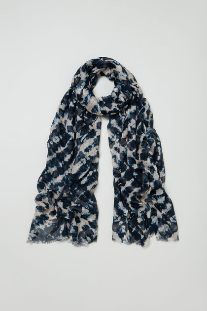 The Diamond Tie Dye Scarf is a long, lightweight modal silk blend with blue, black, and beige abstract patterns, shown loosely looped against a plain white background for a soft, silky drape.