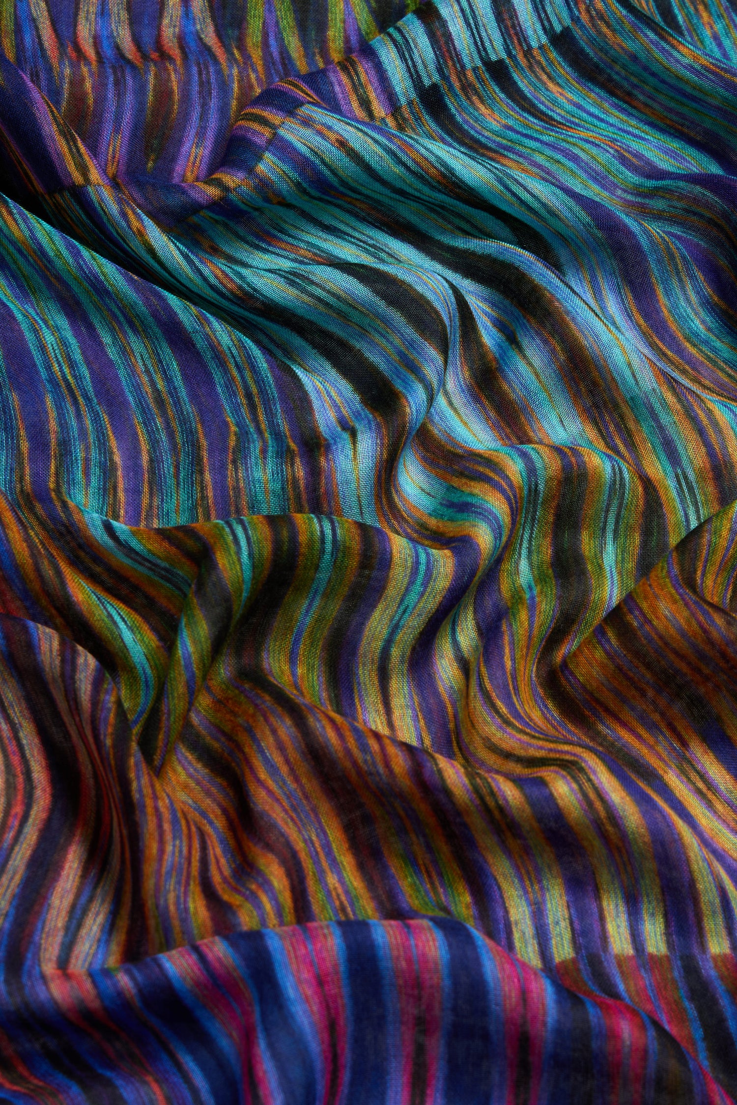A close-up of the Vivid Ikat Patchwork Scarf showcases its multicolored stripes and wavy, flowing texture, capturing the distinct, vibrant appeal of an Ikat pattern.