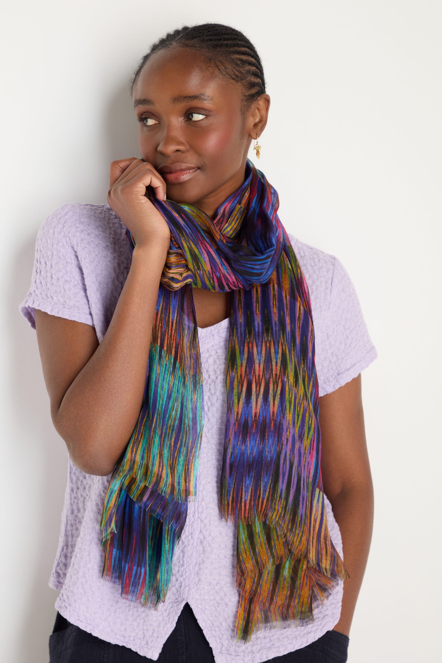Against a white background, a woman gazes to the side wearing a textured lavender top and the Vivid Ikat Patchwork Scarf.