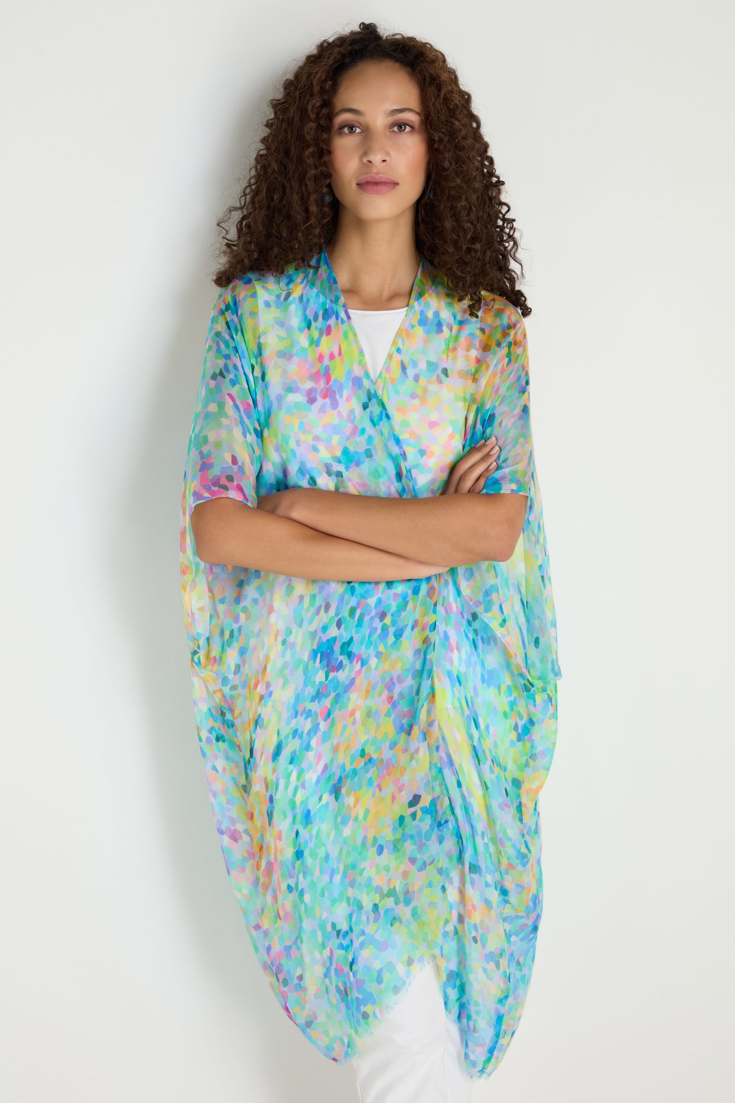 A woman in the Summer Confetti Burst Kimono—a loose, sheer, multicolored layer over a white outfit—stands against a plain light background.