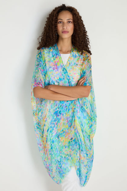 A woman in the Summer Confetti Burst Kimono—a loose, sheer, multicolored layer over a white outfit—stands against a plain light background.