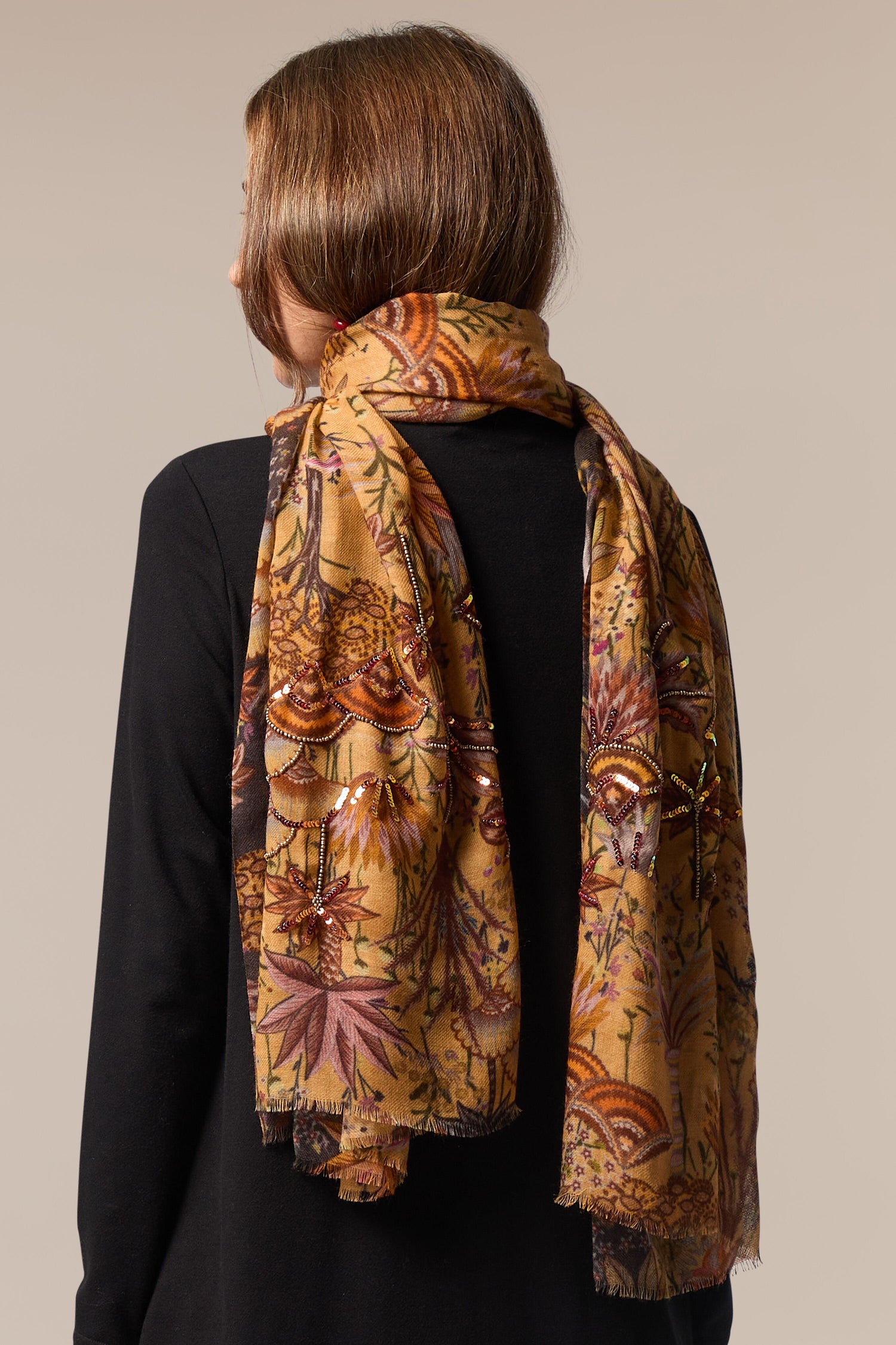 The back view of a woman wearing the Paradise Sequin Detail Wool Scarf with an intricate print.