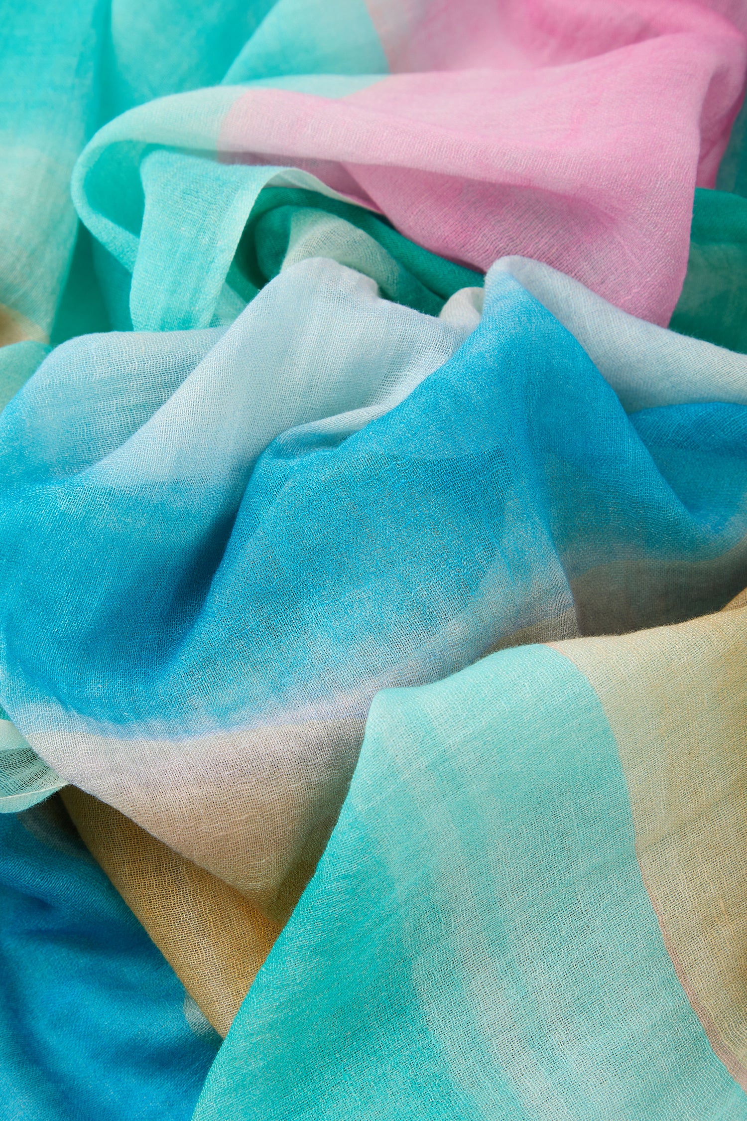 A close-up of the Colour Fusion Scarf shows lightweight, sheer fabric in pastel blue, turquoise, pink, and yellow, softly folded—ideal for adding effortless flair to your summer style.