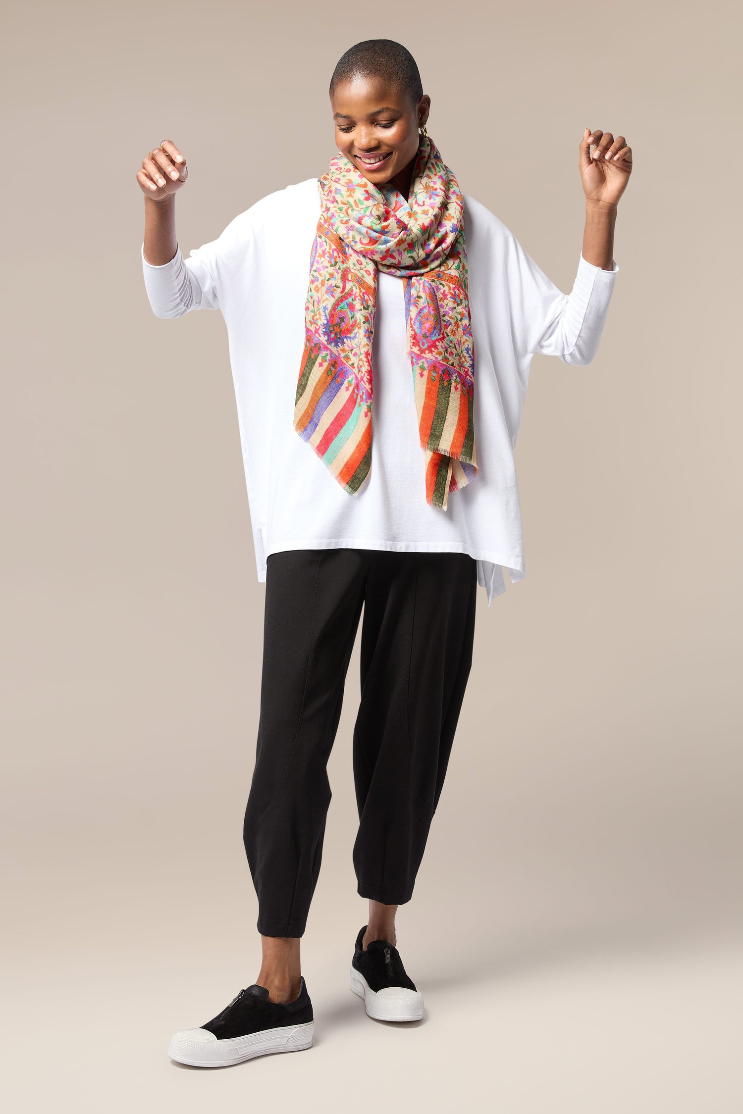 A woman in a white shirt and black pants is wearing an Antique Floral Woollen Scarf as an accessory.