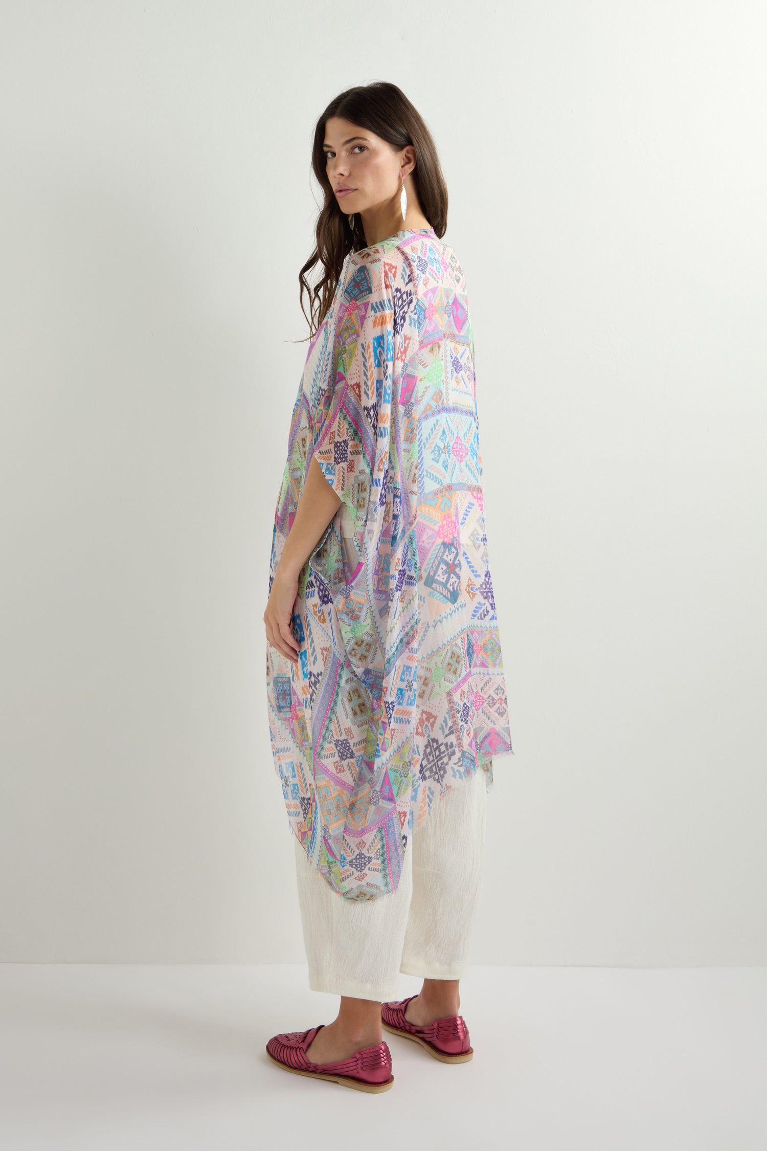 A woman wears the Soft Graphic Patchwork Kimono over white pants and pink shoes, set against a plain backdrop. The lightweight sheer fabric flows gracefully with every step.