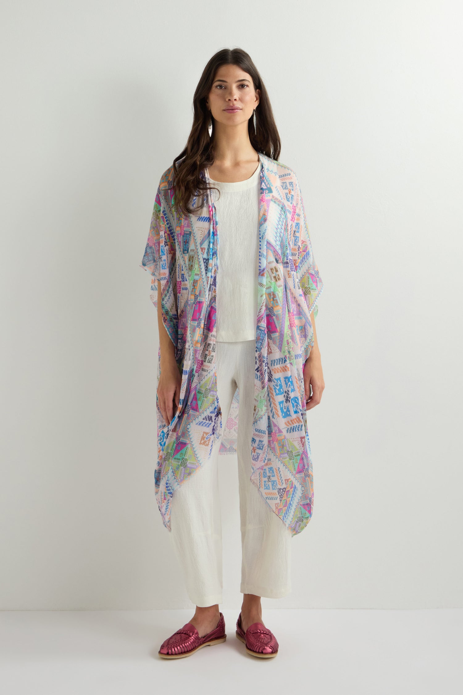 A woman stands against a plain background, wearing a Soft Graphic Patchwork Kimono over a white outfit with red shoes.