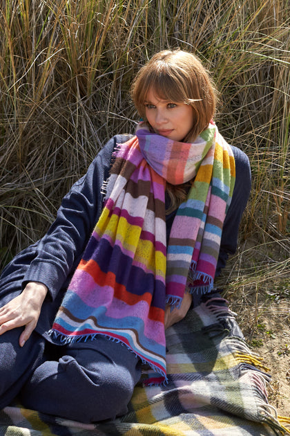 A woman sitting on a blanket with a Rainbow Stripe Cashmere Scarf.