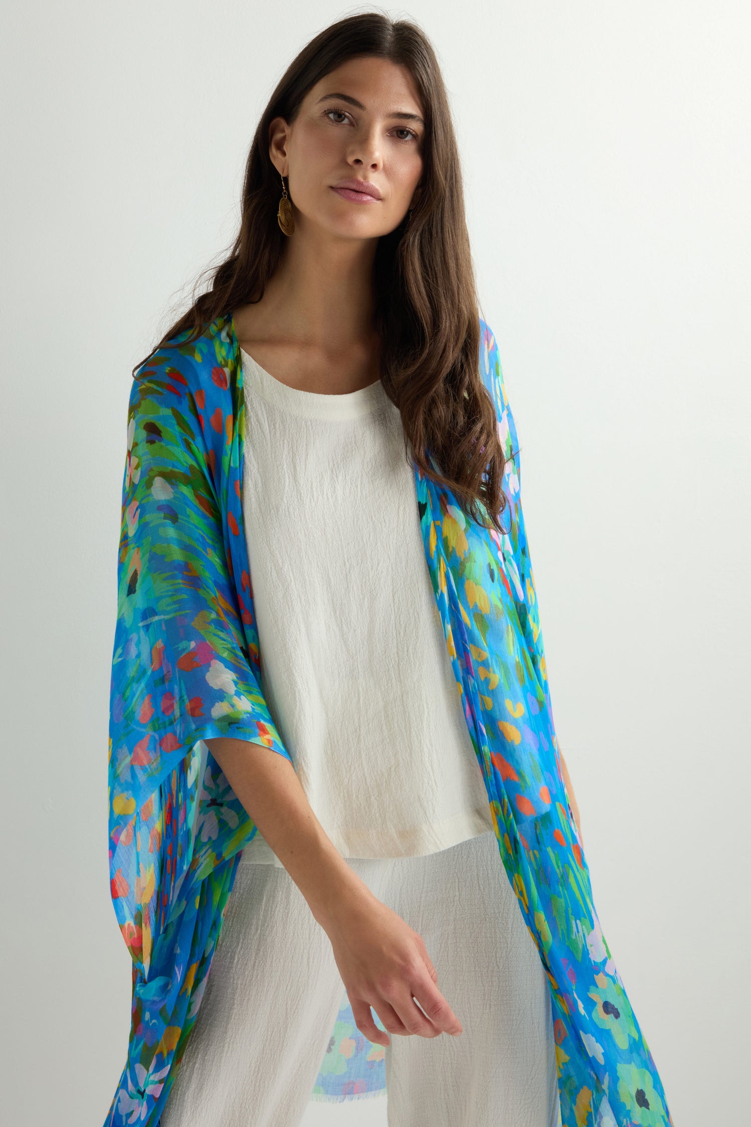 A person in an Abstract Painted Garden Kimono, featuring a flowy open-front silhouette, paired with a colorful floral scarf, stands against a light background.