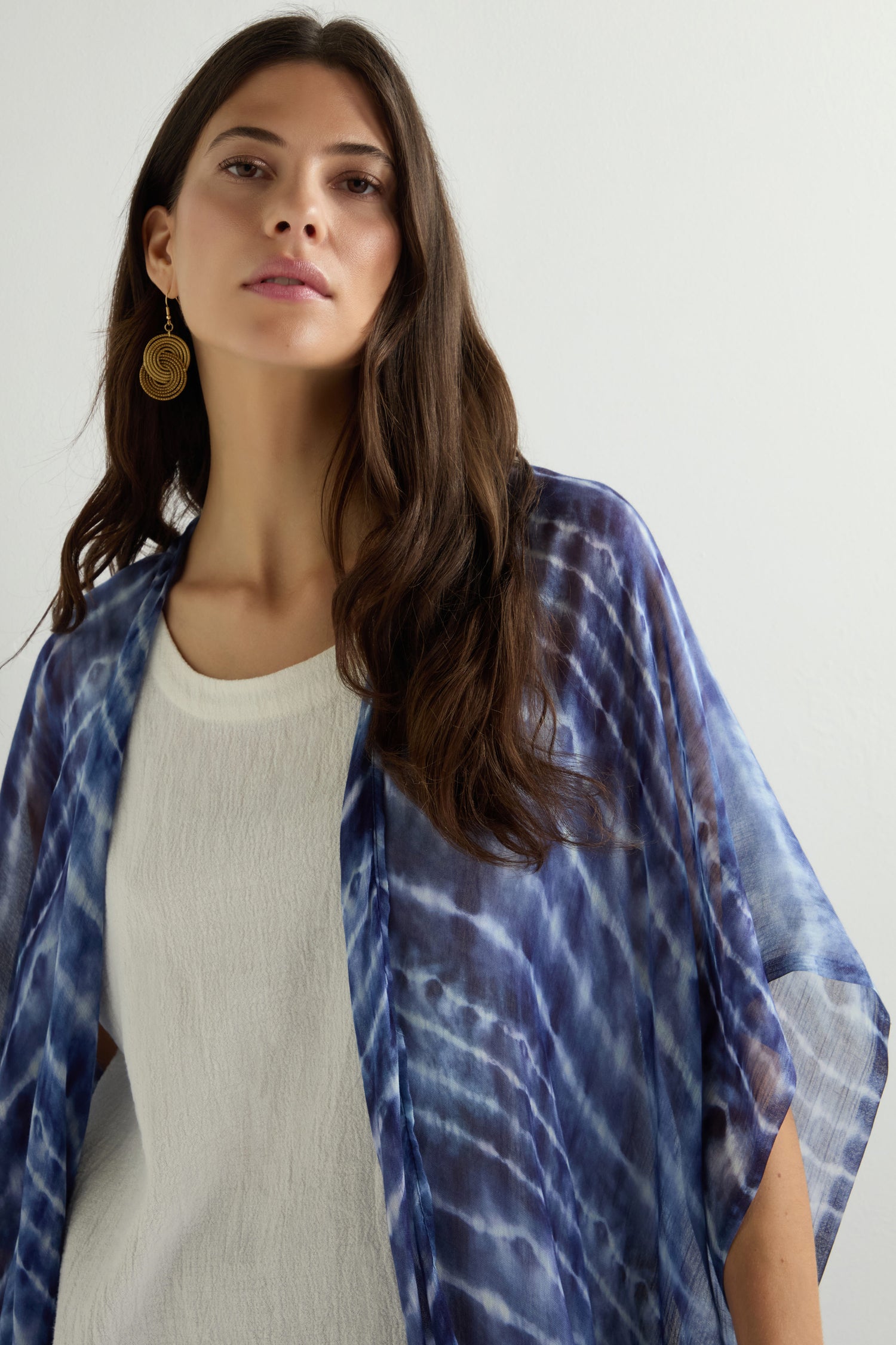 A woman with long hair elegantly models a blue Tie Dye Print Kimono and gold earrings against a plain backdrop.