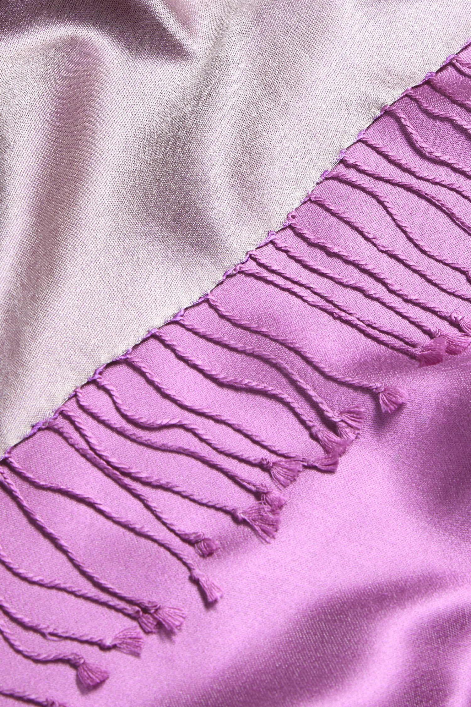 Close-up of the Two Tone Silk Scarf: shiny mauve silk with a luxurious sheen and a row of decorative pink fringe along one edge.