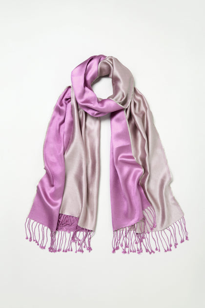 The Two Tone Silk Scarf, made of lustrous silk, showcases a colourblocked design in light purple and lavender with tasseled ends, and is displayed flat on a white background.
