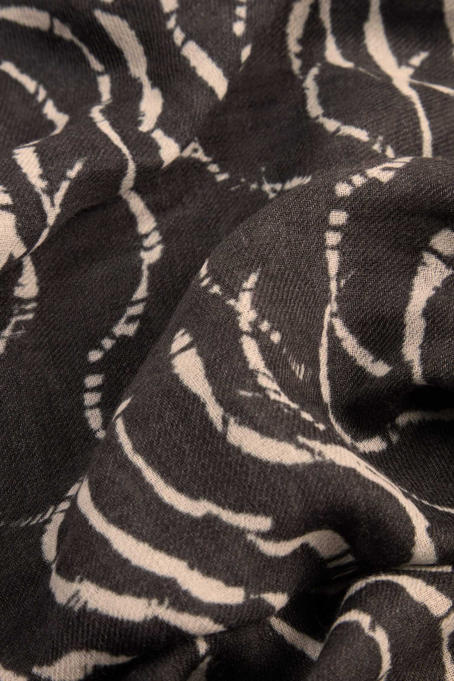 Close-up of the Dancing Waves Scarf, crafted from a wool-silk blend in black and adorned with a white, abstract wavy line pattern. This lightweight winter accessory showcases visible folds and a rich texture.