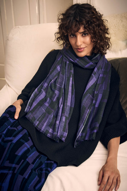 A person wearing a black sweater and a Layered Geometric Wool Scarf with a purple and black geometric print.