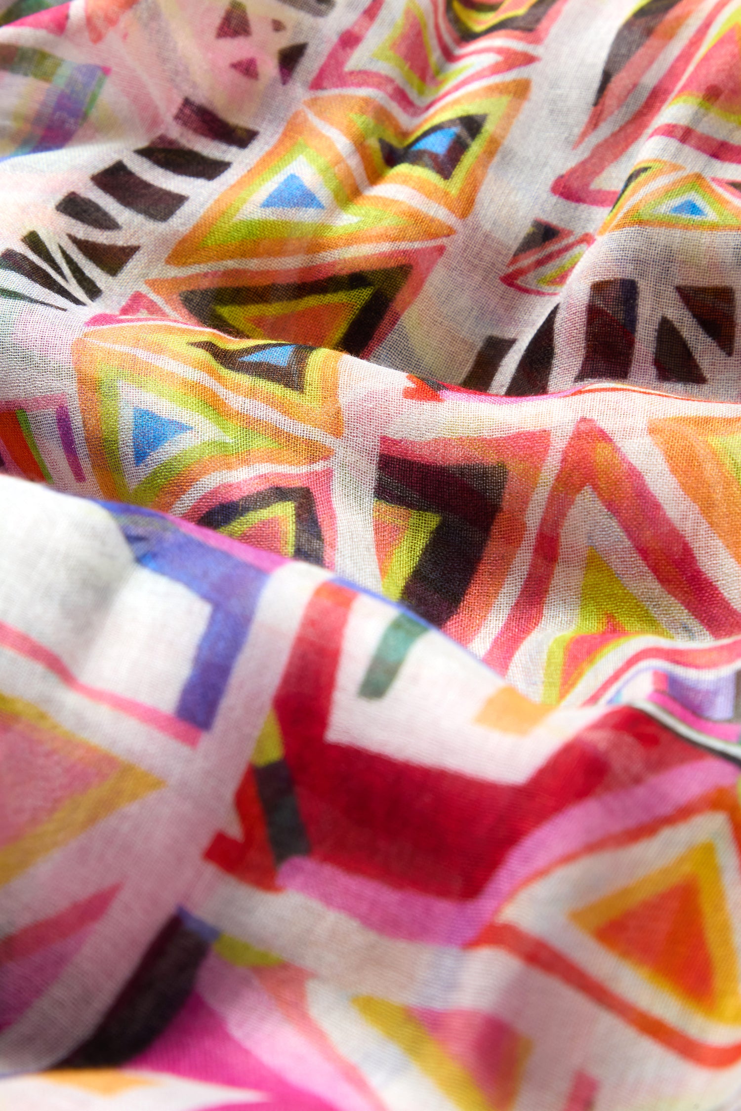 Close-up of the Painted Geometric Scarf, featuring vibrant triangles and lines in yellow, red, pink, green, blue, and black on soft, lightweight fabric with a luxe feel and a slightly wrinkled texture.
