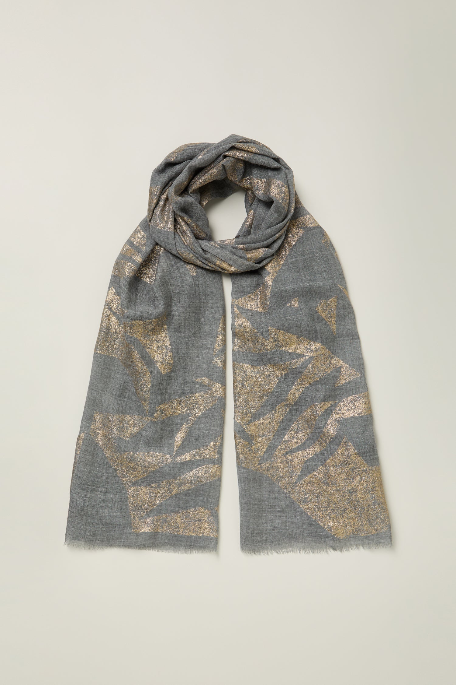 The Aurelian Cotton Scarf in grey displays abstract gold metallic patterns, lightly folded and laid flat on a light background.