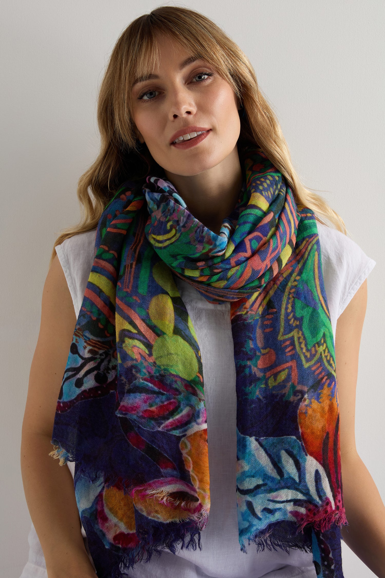 Woman wearing a white top and the Painted Paisley Wool Scarf—a colorful, lightweight wool scarf with a paisley design—stands against a plain light background.