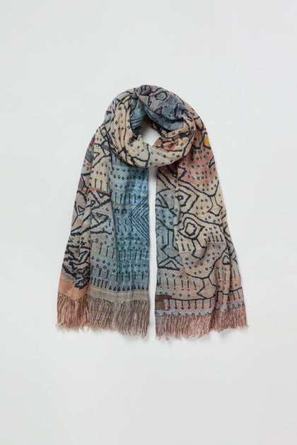 The Sketch Mountain Wool Scarf is a lightweight wool accessory showcasing geometric and abstract print designs in blue, beige, and brown tones, accented with fringed ends and displayed laid flat against a white background.