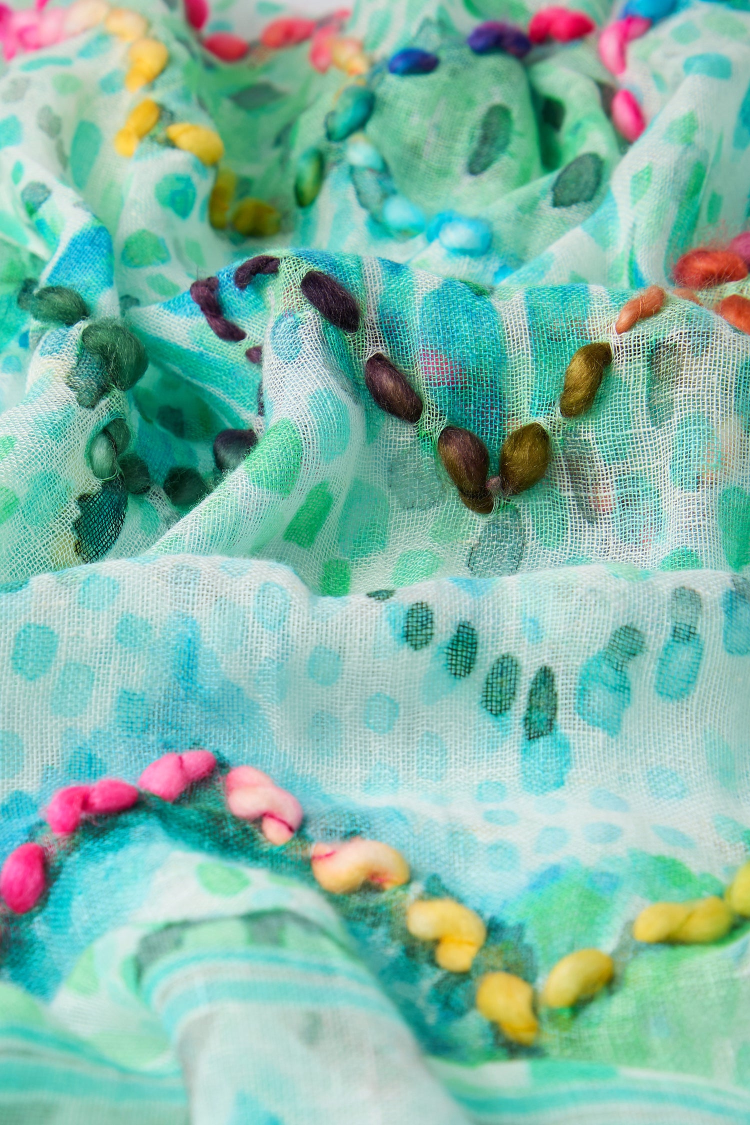 A close-up of the textured green fabric on the Embroidered Zig Zag Stitch Scarf, featuring colorful bead-like embellishments scattered across, evokes an artistic charm.