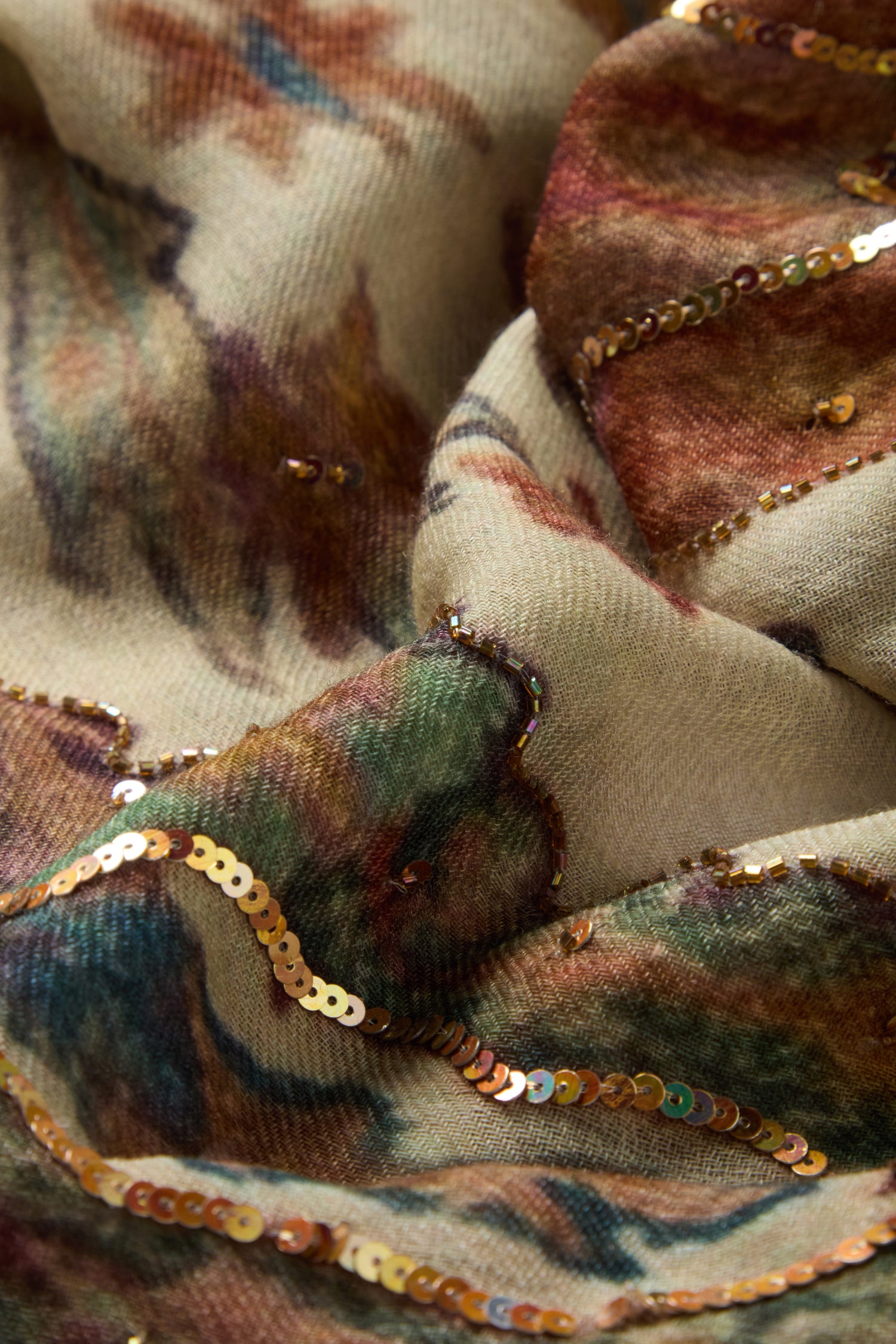 Close-up of the Embroidered Tapestry Wool Scarf, showcasing beige wool fabric adorned with a multicolored pattern and gold sequin embroidery in wavy lines, creating a richly textured and shimmering surface.