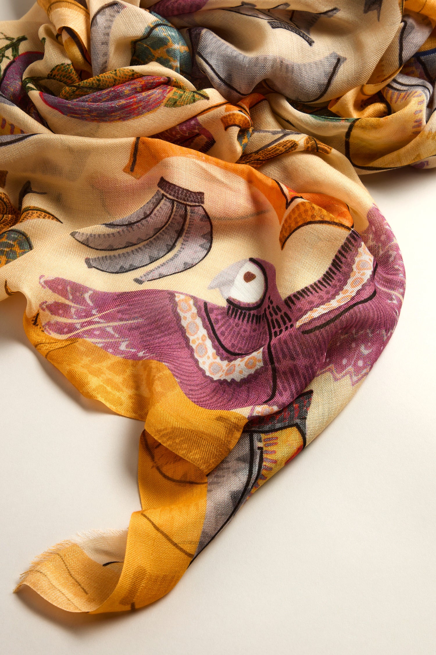 The Bird of Paradise Modal Scarf features ultra-soft modal fabric adorned with vibrant bird designs in purple, orange, and yellow hues. Its exquisite drape evokes the allure of tropical landscapes.