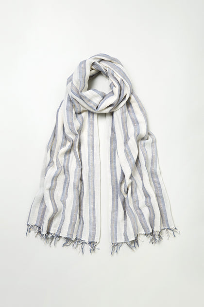 The Lurex Stripe Cotton Blend Scarf is lightweight and breathable, with vertical blue, grey, and white stripes and fringed edges, shown laid flat on a plain background.