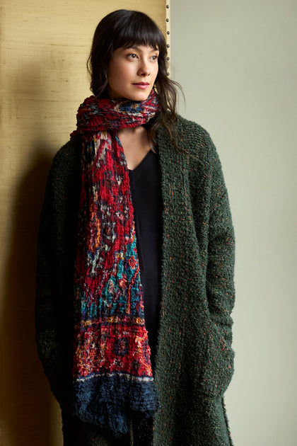 A person wearing a Crushed Sequin Detail Wool Scarf with ruby-toned, light-reflecting embellishments over a dark green sweater.