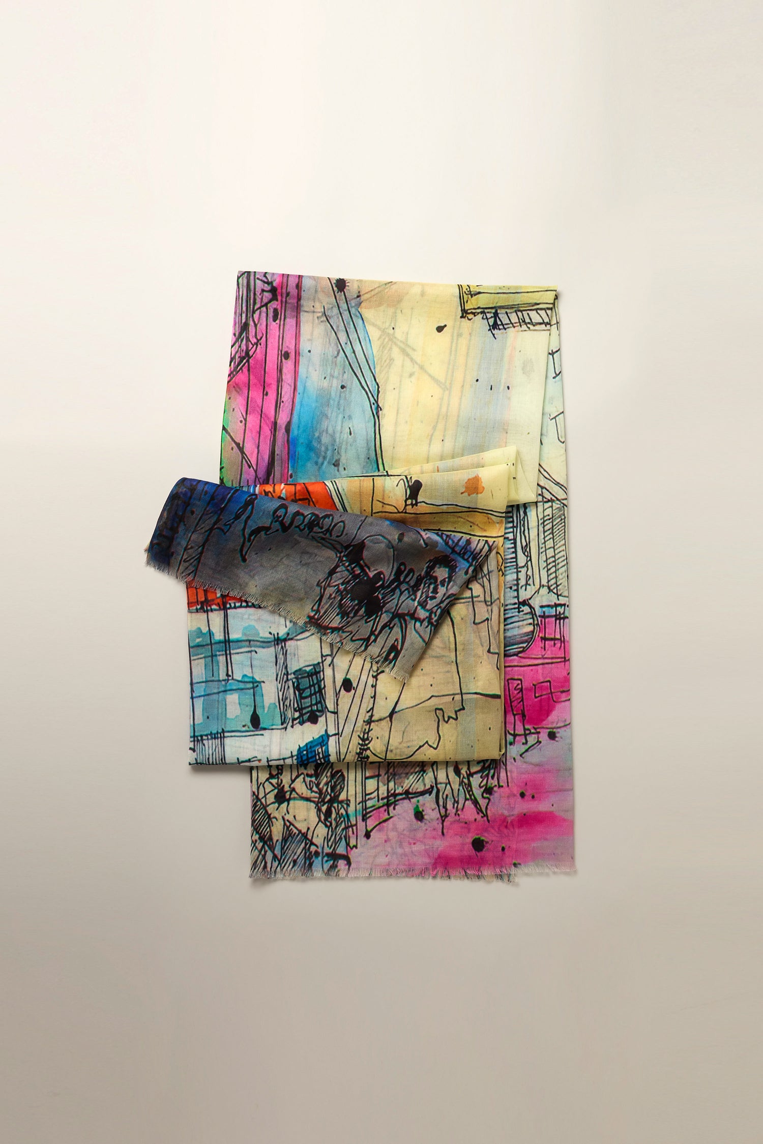 Three pieces of cloth with abstract, colorful patterns and sketch-like designs are neatly stacked against a plain backdrop, embodying the spirit of the Abstract City Sketch Cotton Modal Scarf.