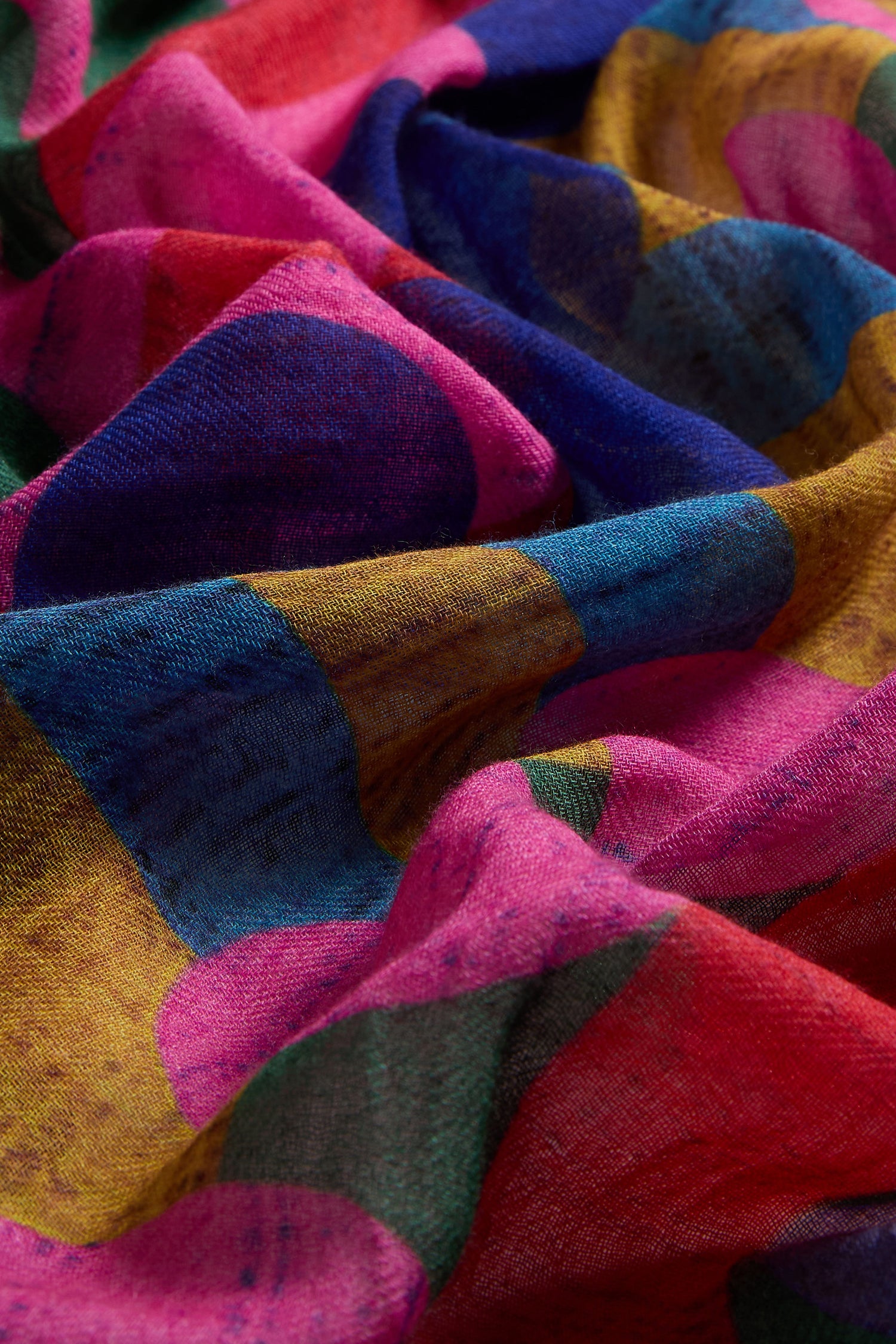 A close-up of the Colour Pop Circles Wool Scarf, showcasing its abstract design with bold pink, yellow, blue, and red sections in a textured wool-silk blend, visible weave details, and gentle folds.