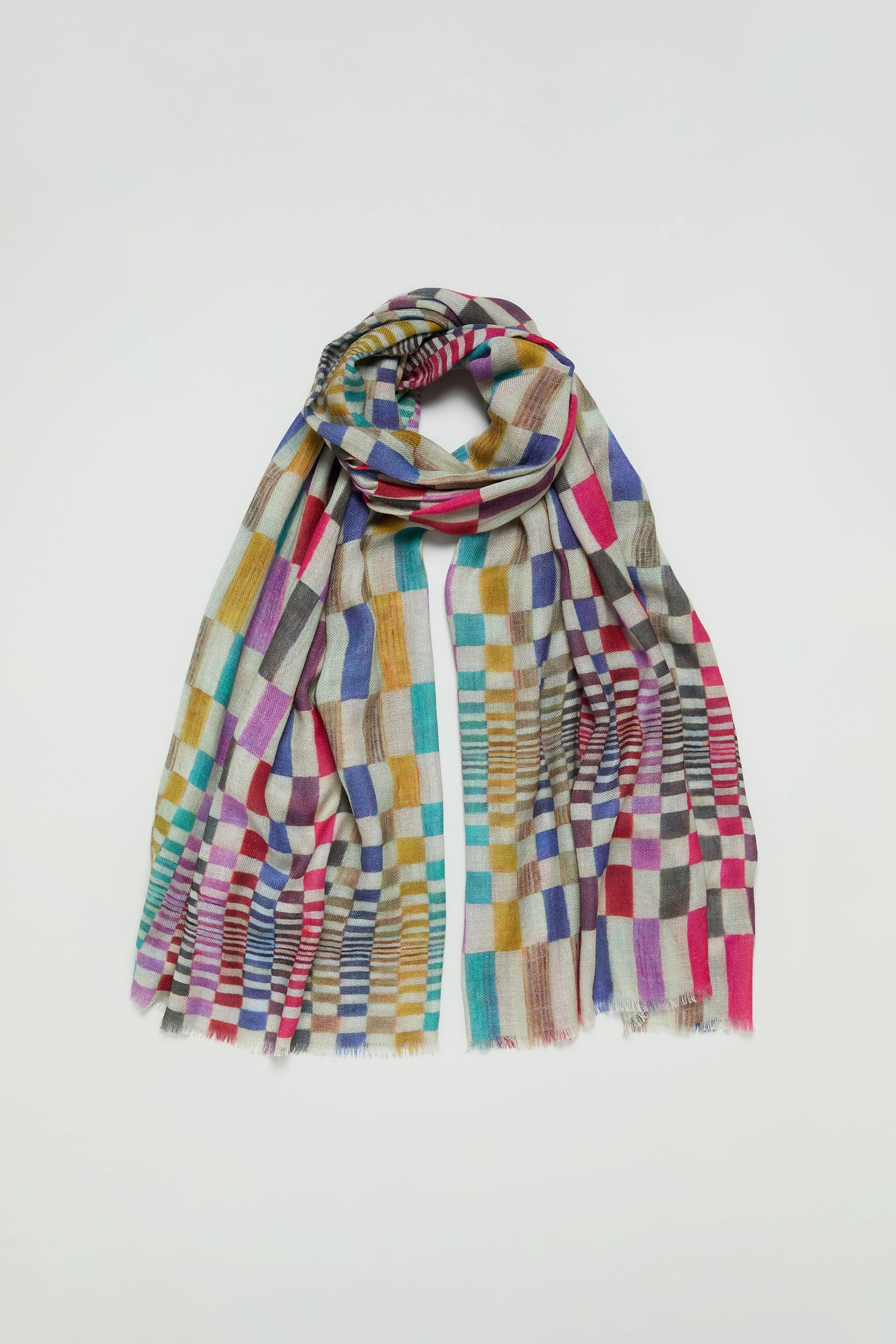 The Mirage Check Wool Scarf showcases a vibrant checkered pattern in red, blue, yellow, green, and beige hues, set against a plain white background.