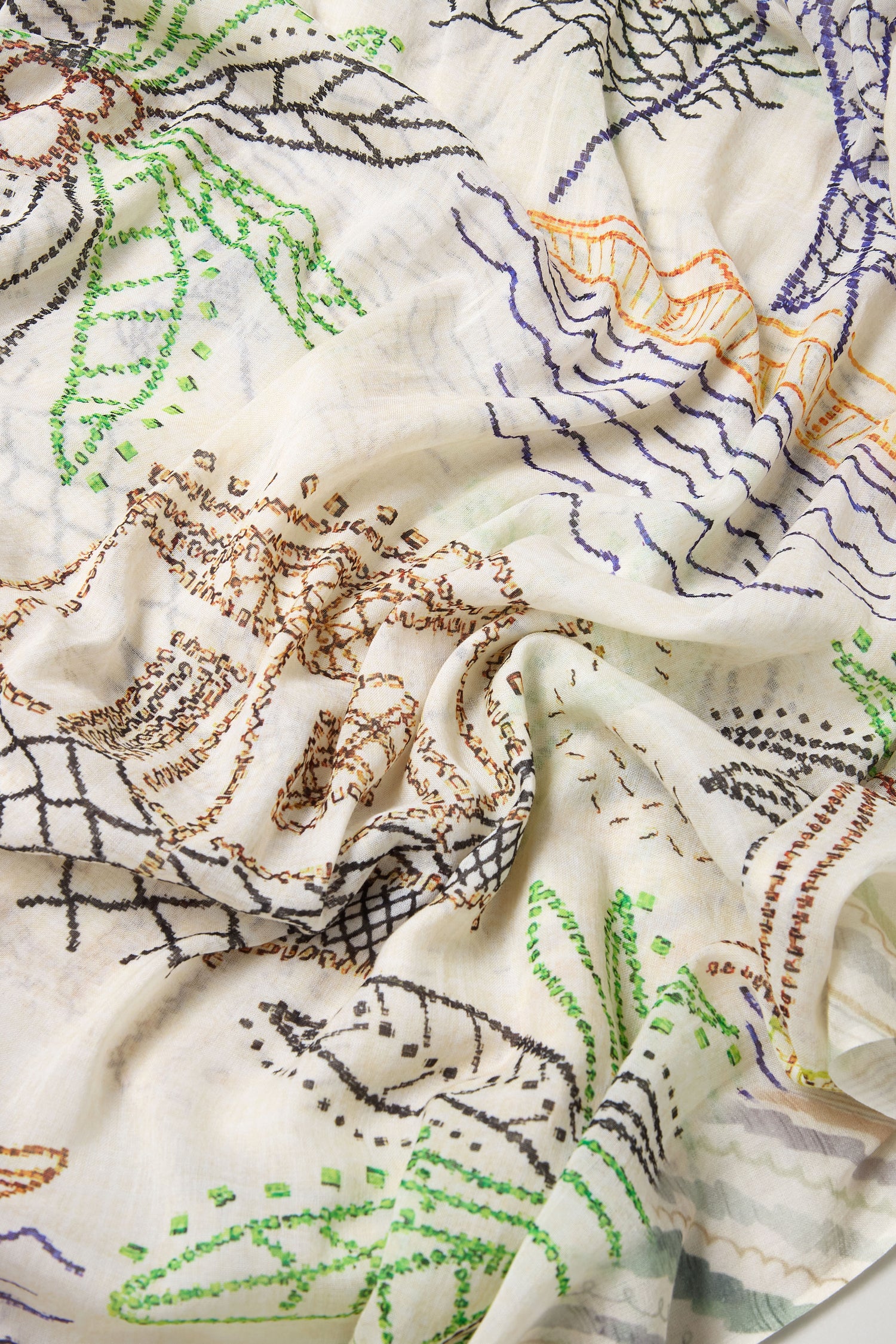 A close-up of the By The Sea Cotton Modal Scarf shows white, lightweight, breathable fabric with multicolored stitched embroidery in green, brown, black, orange, and purple.