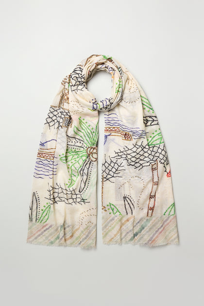 The By The Sea Cotton Modal Scarf is lightweight and breathable, featuring abstract multicolored stitched designs inspired by plants, lines, and coastal motifs, set against a plain background.