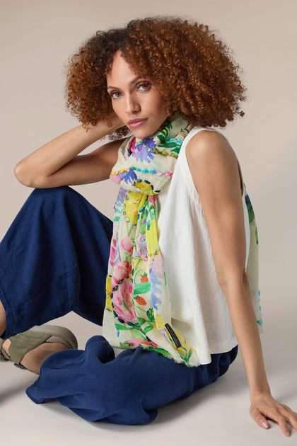 A woman with curly hair and a Meadow Embroidered Scarf sitting on the floor.