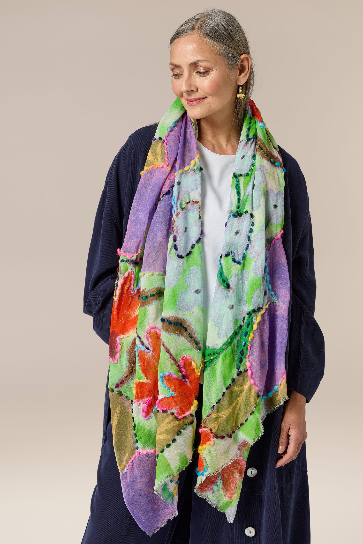 A woman wearing a Wild Garden Embroidered scarf with an abstract floral pattern.