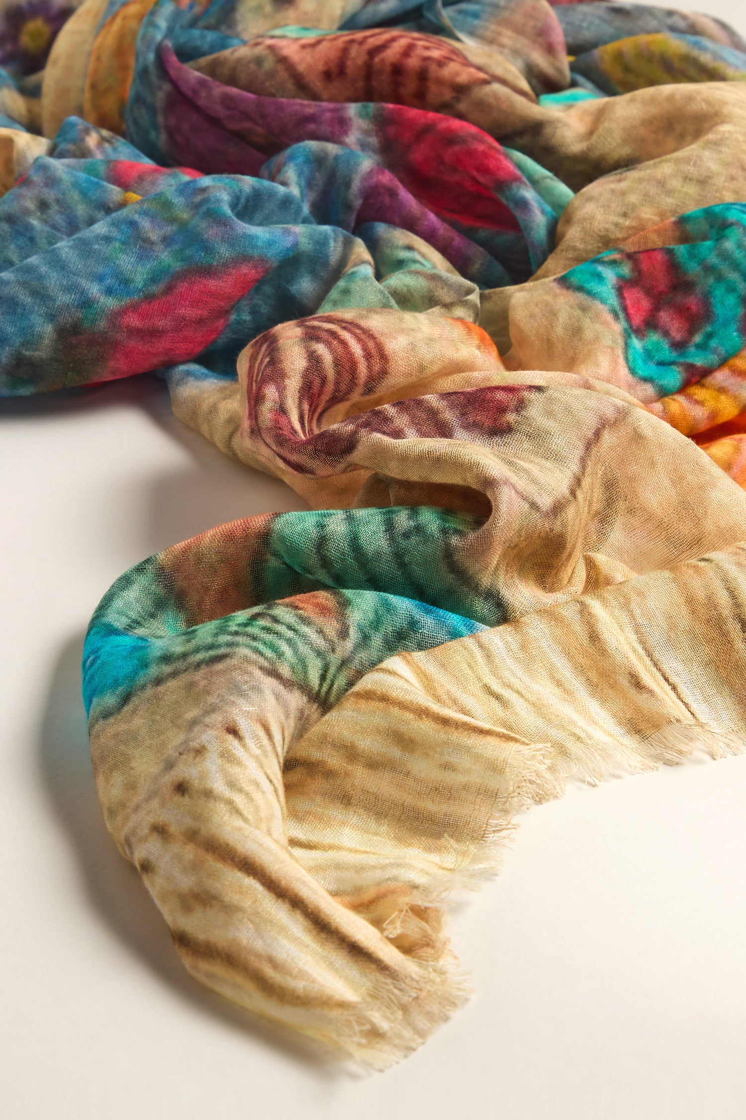 The Riverside Cotton Mix Scarf displays a vibrant blend of blue, red, yellow, and green hues on a white surface, ensuring lightweight comfort with its breathable cotton mix.