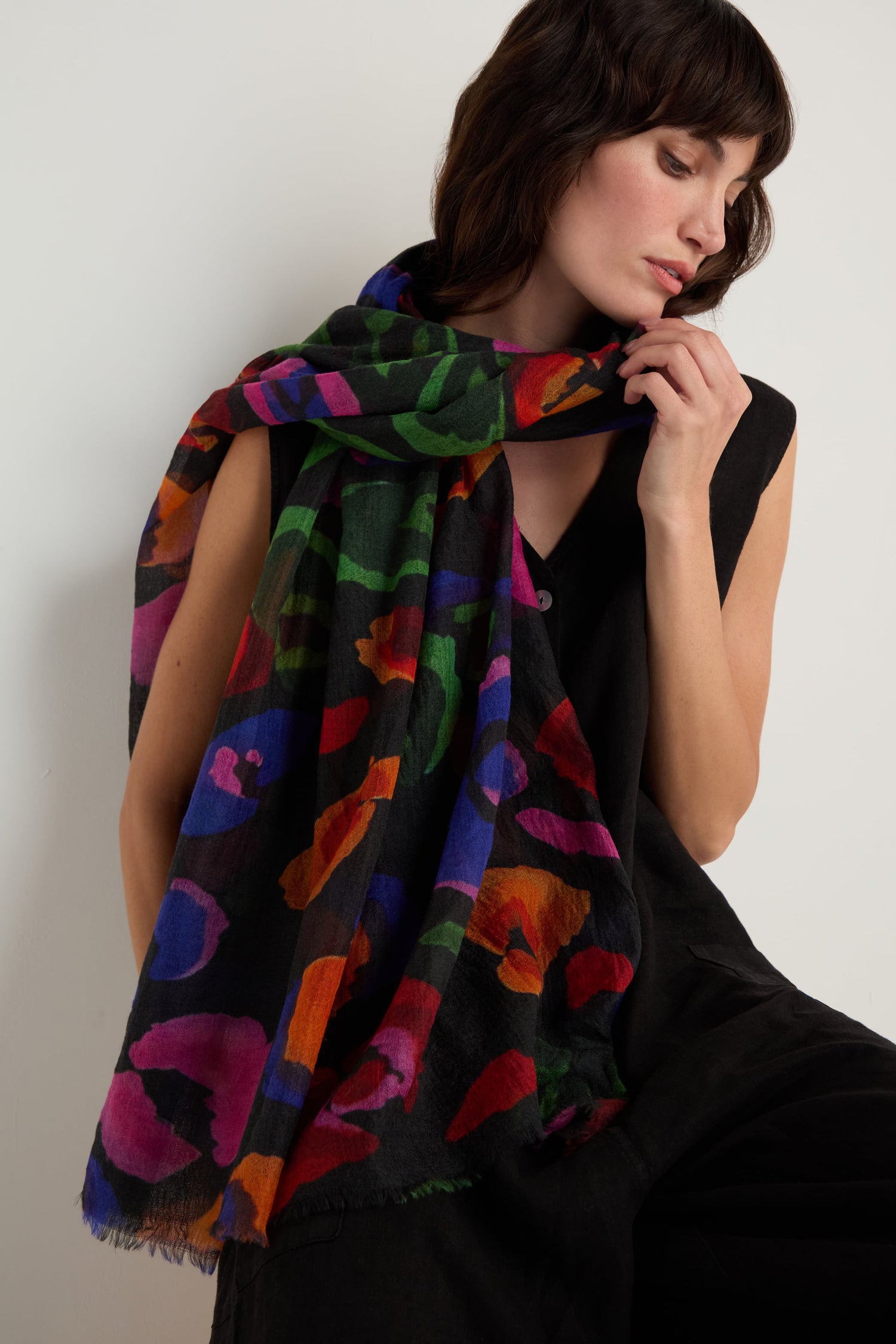 A woman wearing a sleeveless black outfit has the Painted Pansy Wool Scarf with a vibrant multicolour pansy print draped over her shoulders, looking down.