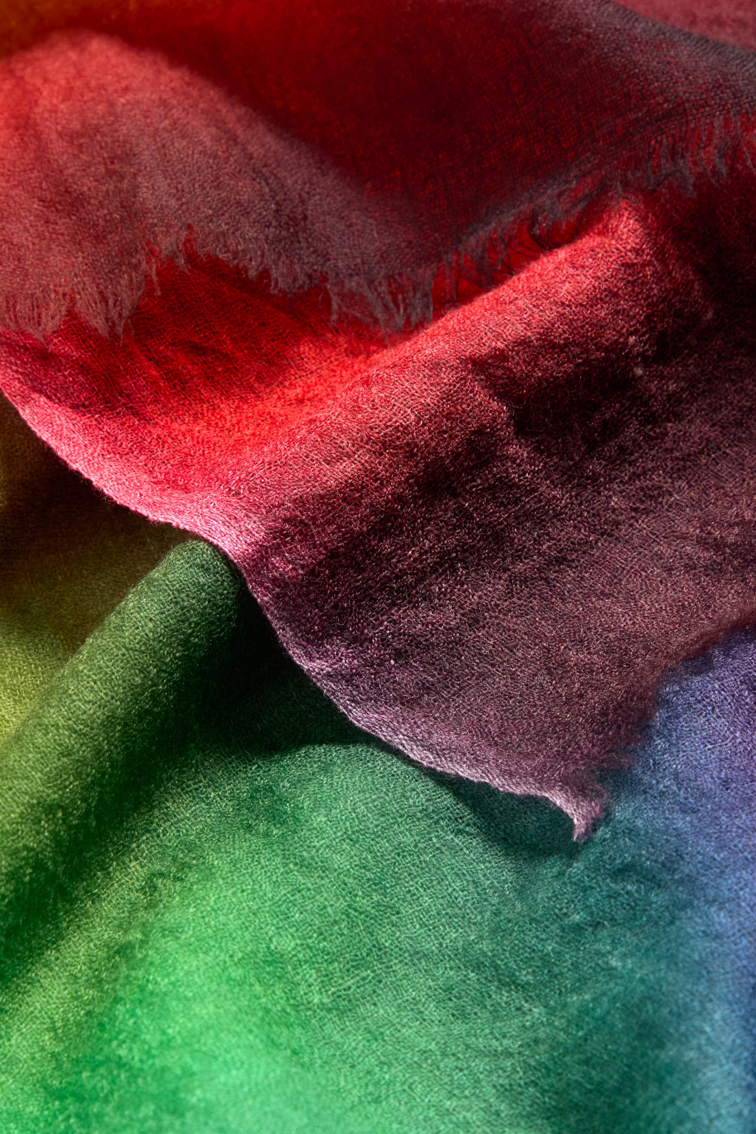 A close-up of soft, textured fabric with a vivid gradient of red, purple, green, and blue reminiscent of the Aurora Wool Scarf.