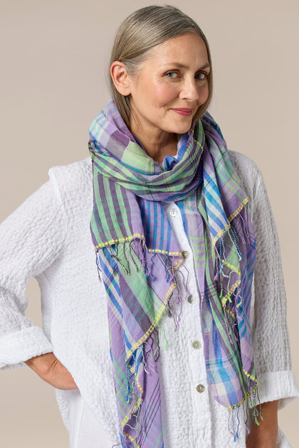 A woman accessorized with a Check Stitch Cotton Scarf in shades of purple and green.