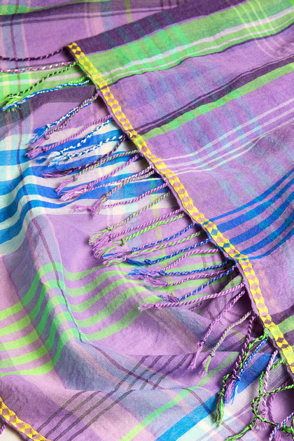 The Check Stitch Cotton Scarf features a vibrant woven design with colorful stripes in purple, blue, green, and yellow. Charming fringed edges enhance this delightful accessory.