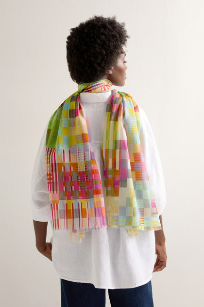 Against a plain backdrop, a person viewed from behind wears a light shirt complemented by the elegantly draped Rainbow Checkerboard Cotton Modal Scarf over their shoulders.