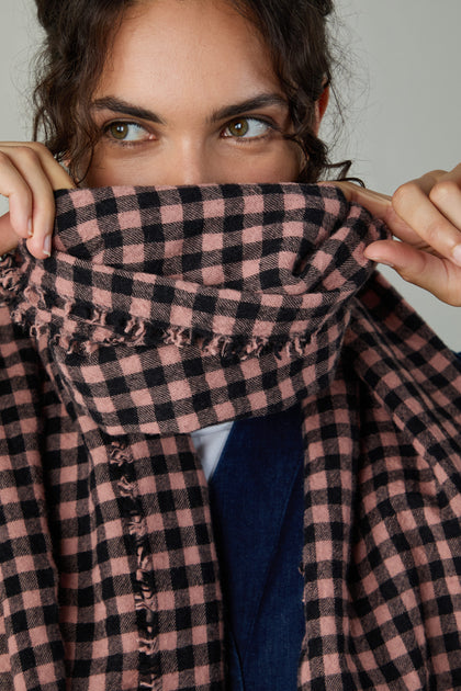 A person holds the Boiled Wool Gingham Check Scarf over the lower half of their face, revealing only their eyes and forehead and showcasing the scarf's lightweight warmth and stylish gingham design.