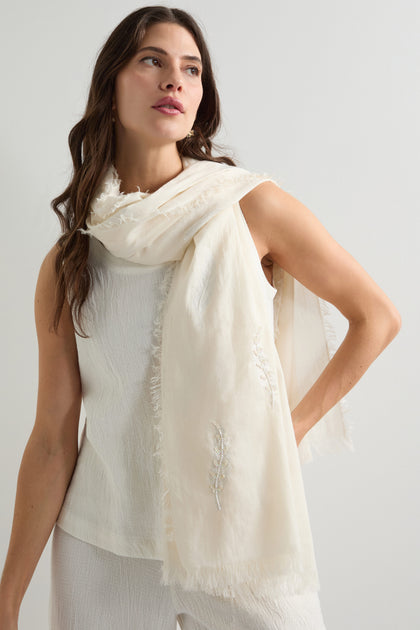 Against a plain background, a person in white top and pants elegantly drapes the Hand Embroidered Feather Scarf around their neck.