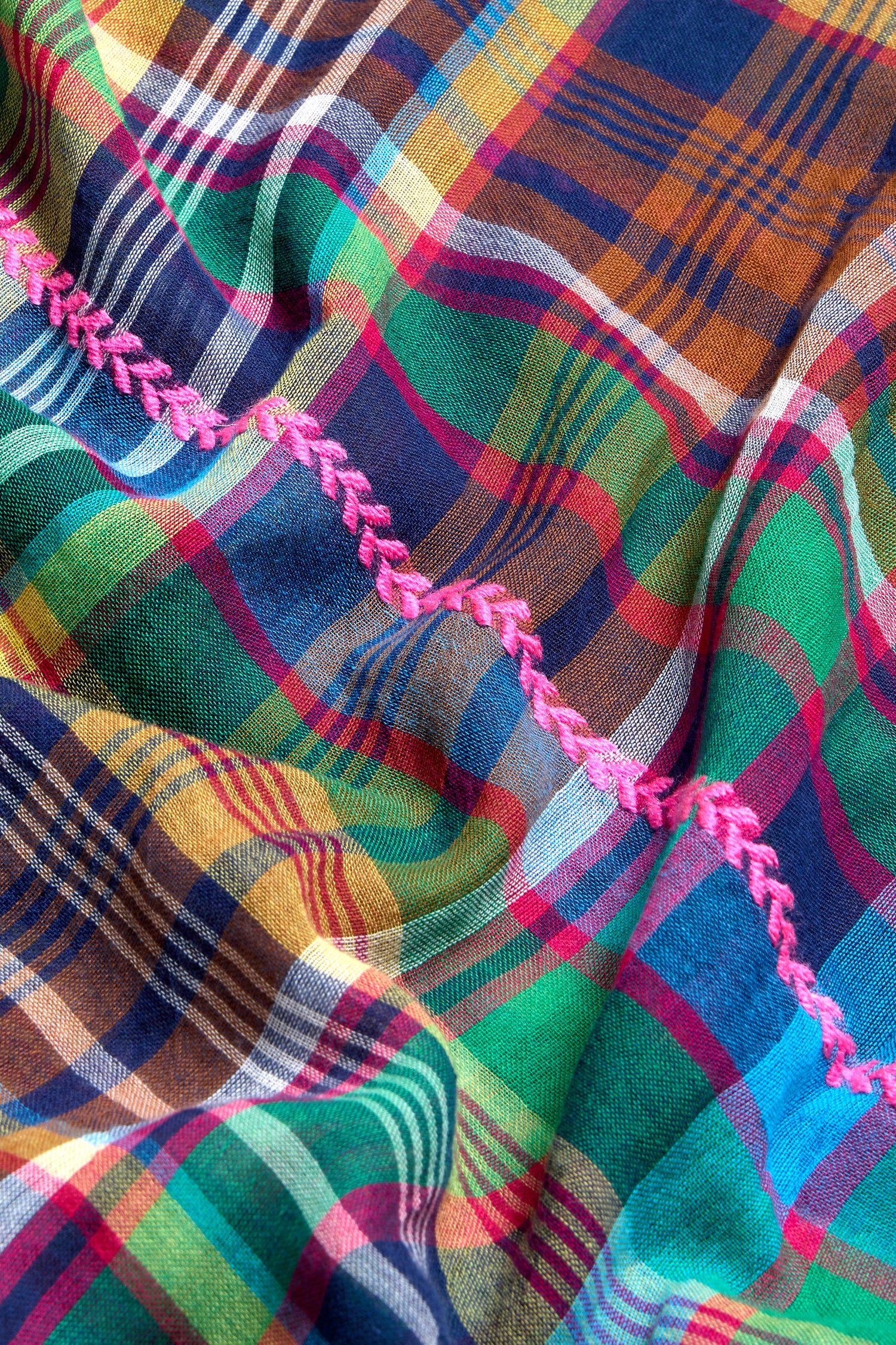 A close-up of the Fuchsia Embroidered Check Scarf showcases its colorful check pattern with blue, green, yellow, and red lines and a pink zigzag stitch—an ideal cotton blend scarf for adding a vibrant accent.