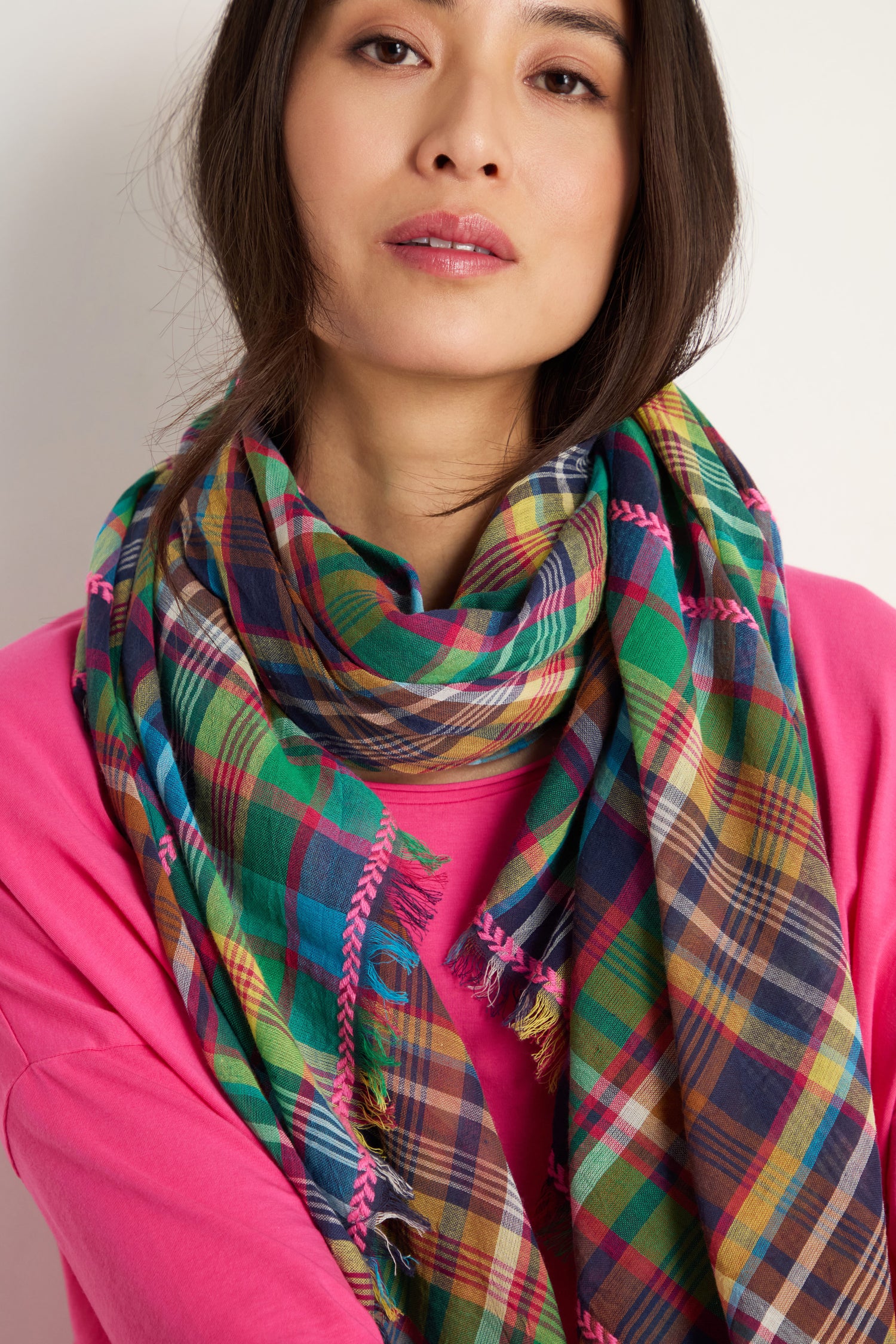 A person in a pink top and a Fuchsia Embroidered Check Scarf made from a cotton blend checked fabric looks at the camera with a neutral expression.