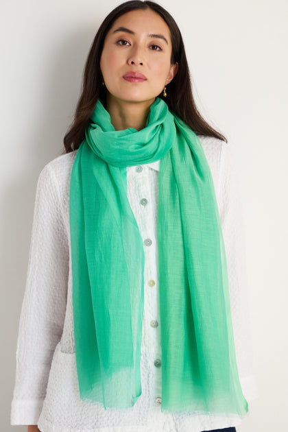 A woman wearing a white textured button-up shirt and the Verdant Cotton Blend Scarf in light green stands against a plain light background.