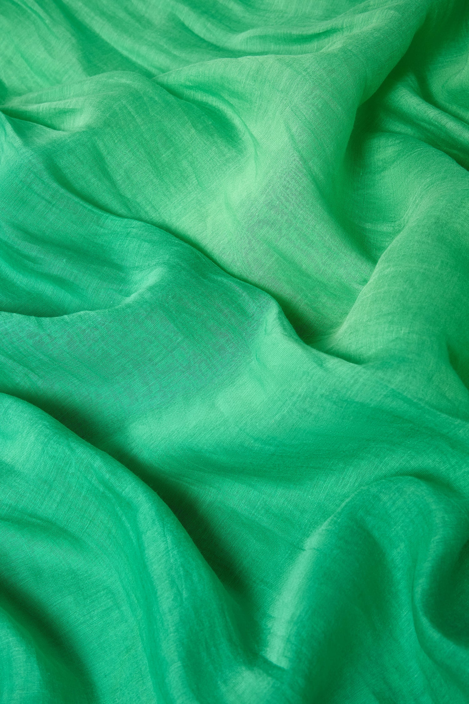 A close-up of the Verdant Cotton Blend Scarf showcases its green fabric, lightweight feel, visible texture, and soft folds that create a graceful, flowing pattern.