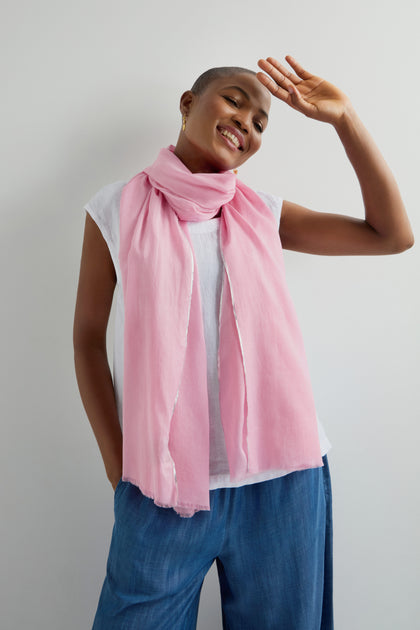 A person smiles, dressed in a white shirt, blue pants, and a Silver Edge Cotton Scarf from our collection, standing against a plain white background.